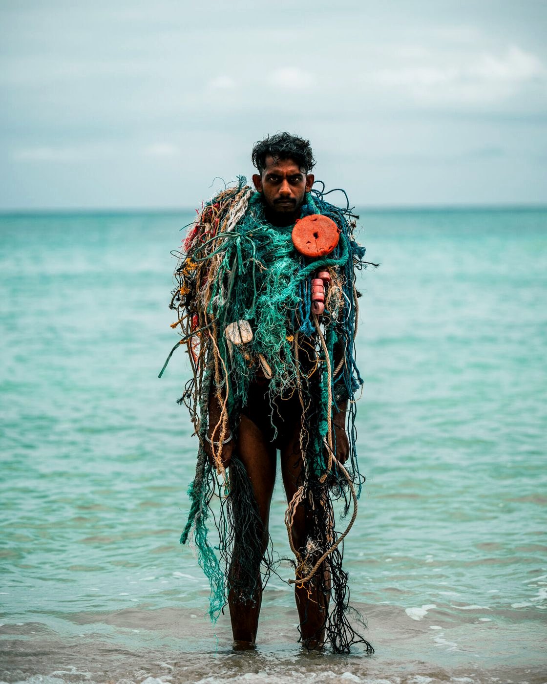Diver standing in shallow water wrapped in ghost net with an orange float